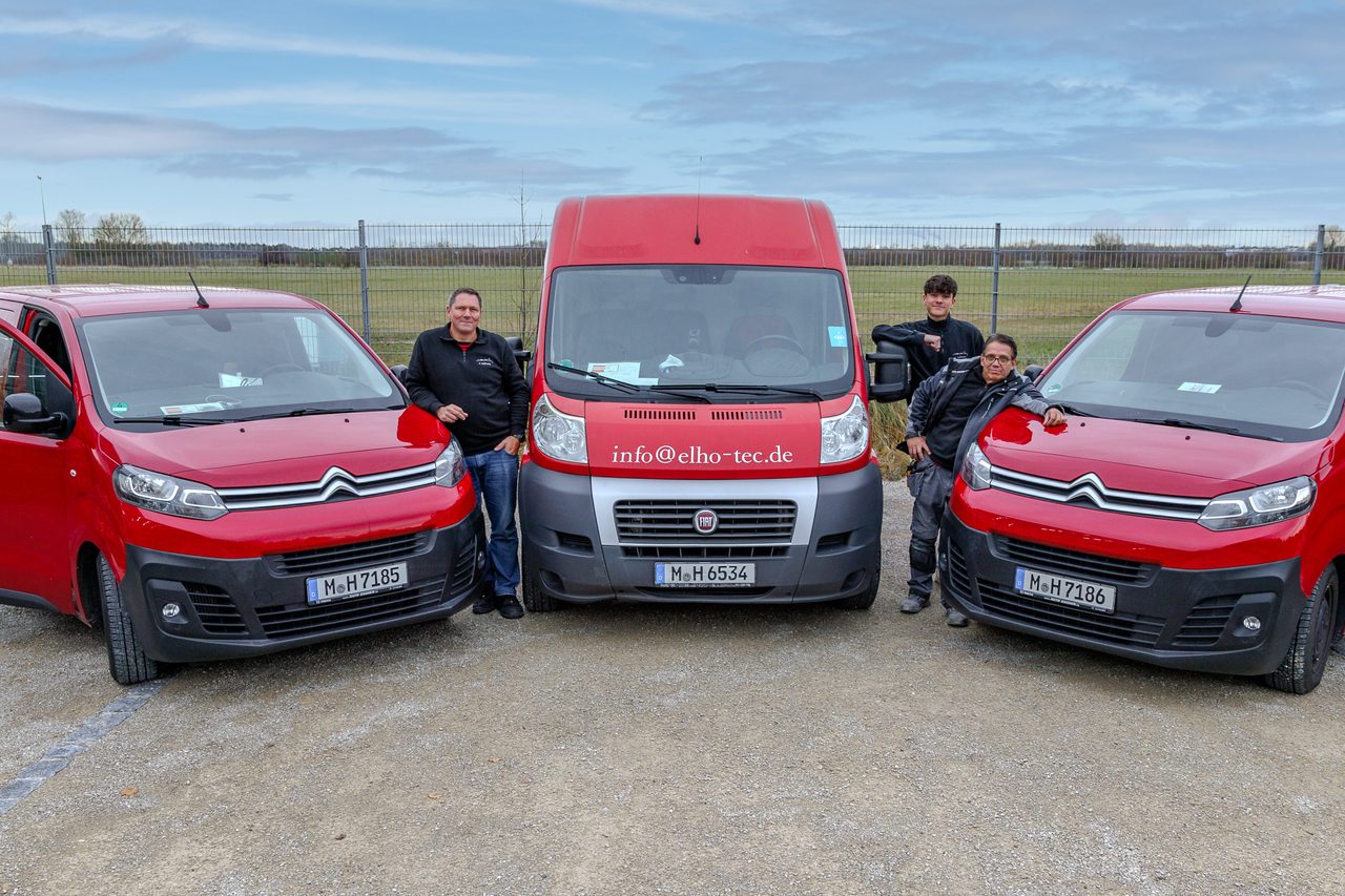 Der Fuhrpark der elho-tec GmbH mit drei roten Servicefahrzeugen und dem Team