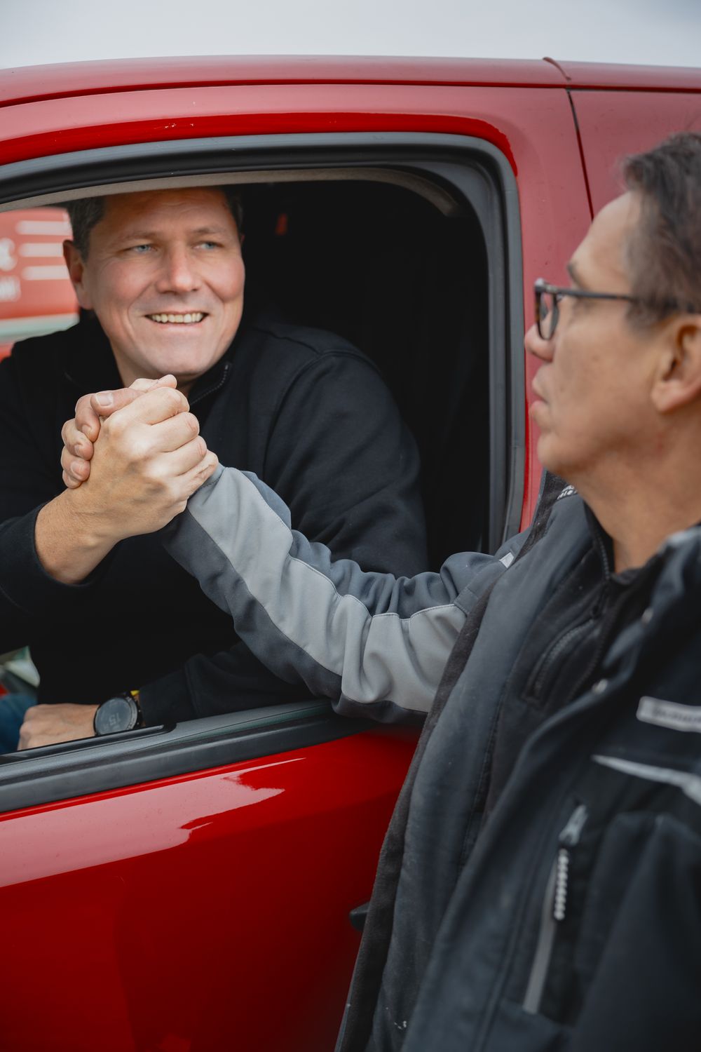 Zwei Personen besiegeln per Handschlag durch das Fenster eines roten elho-tec-Servicefahrzeugs die Zusammenarbeit